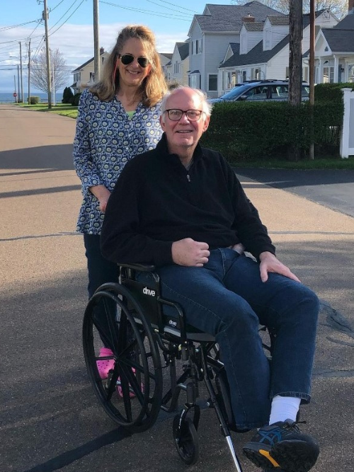 Lisa and Mike Foster outside in Old Saybrook, CT. Lisa is pushing Mike in a wheelchair because he had lasting side effects from a stroke.