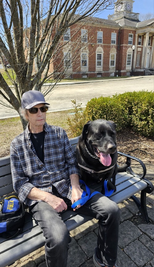 Alan Smith sitting on a bench outside with Beaux, his LabRottweiler dog. 