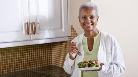 older woman eats a salad while smiling