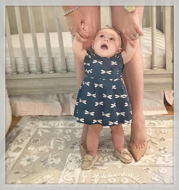 infant stands holding mom's hands