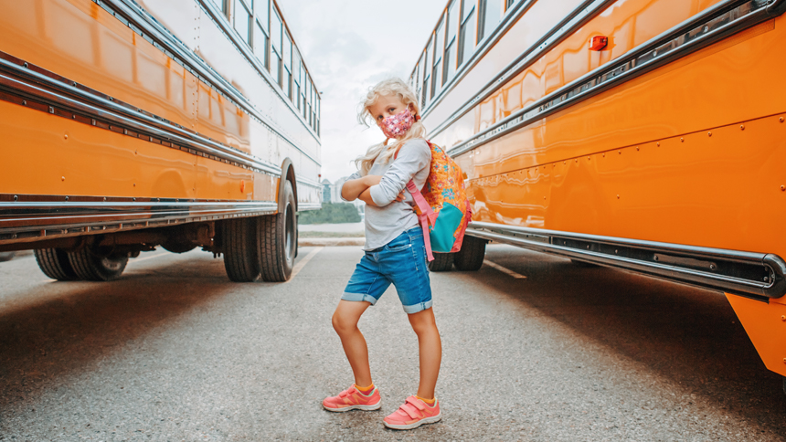 Child stands next to school buses