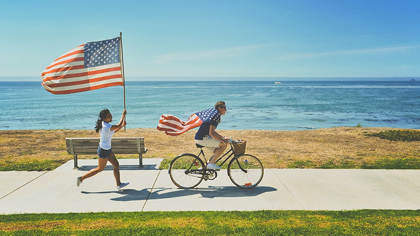 two people, one on a bicycle and one running behind. Both have American flags.