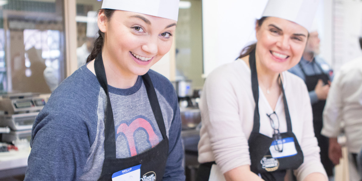 Two women in a cooking class, looking at the camera.