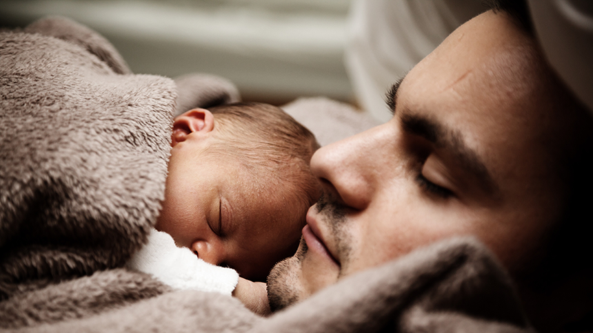 A close-up shot of a father laying down and holding his newborn on his chest.