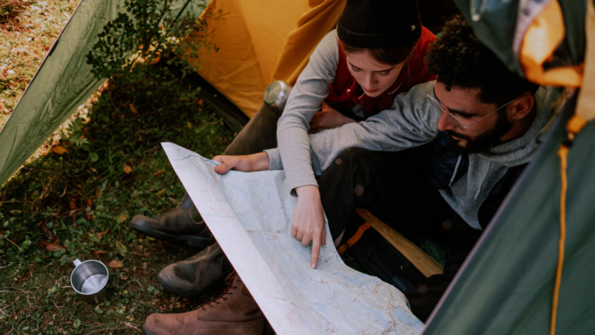 A photo of a couple sitting in a tent looking at a map.