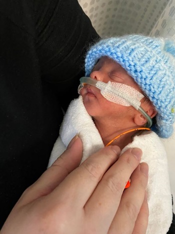 Premature baby in blue hat held by mother