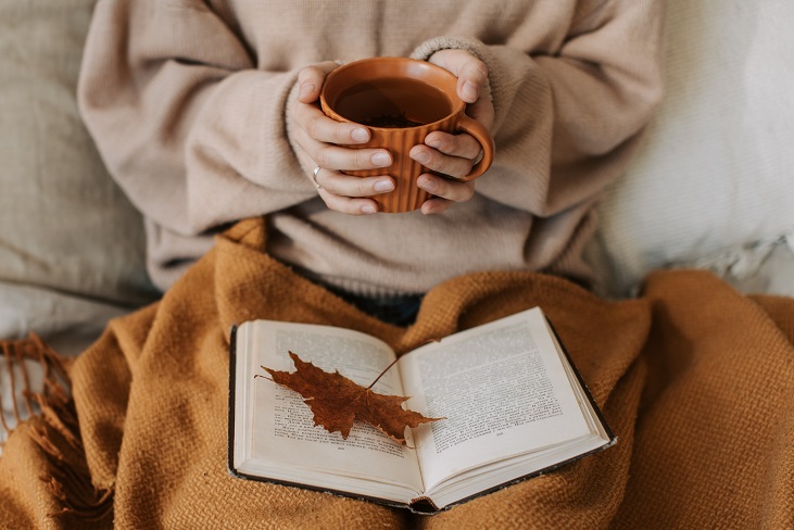 Woman sitting while holding a cup of tea and reading a book.