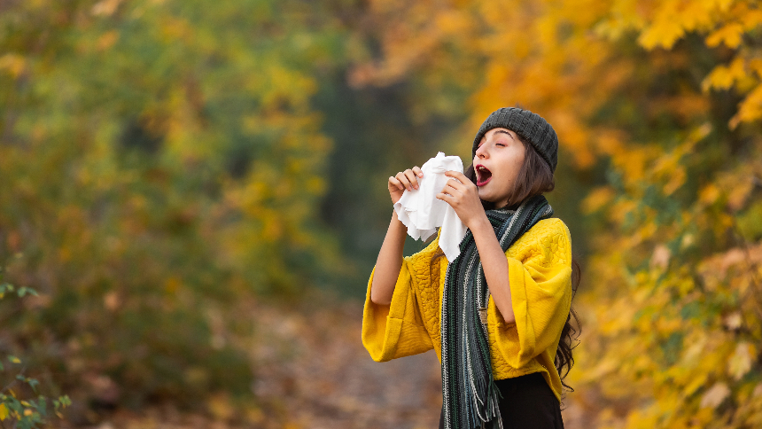 Girl sneezes into a headscarf in autumn in the park. Allergies can trigger migraines.
