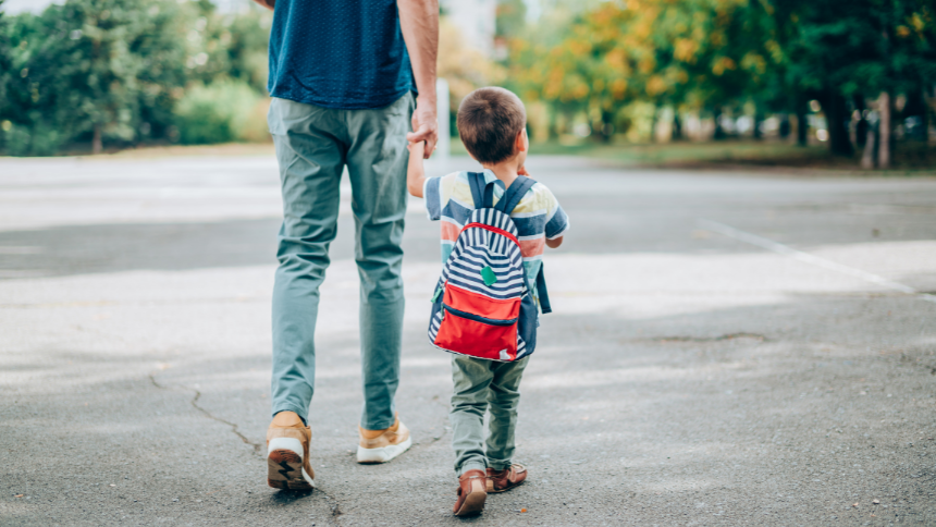 Young dad walks young son wearing a backpack to school
