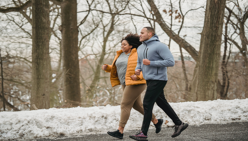 Woman and man jogging outside on the road with snow on the ground. 