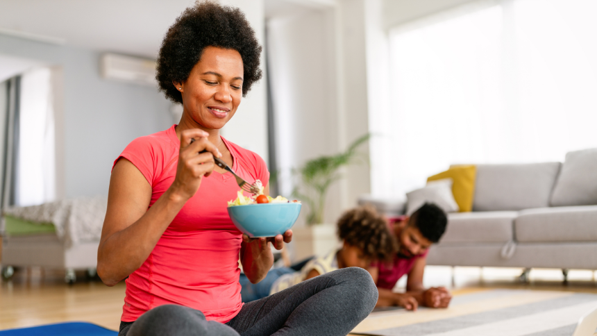 African American woman with family on background eating a healthy salad after workout. Fitness and healthy lifestyle concept.