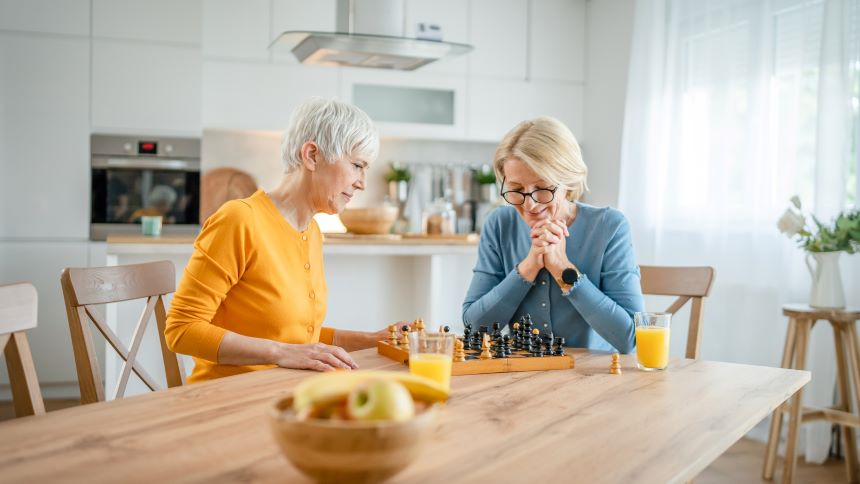 Two senior women playing chess board game at home in the kitchen.