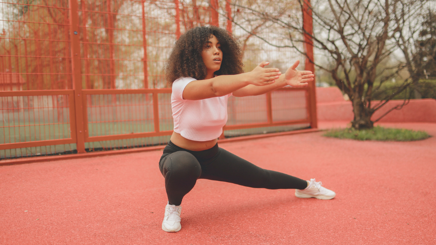 Young woman doing a side lung stretch outside on a track. 