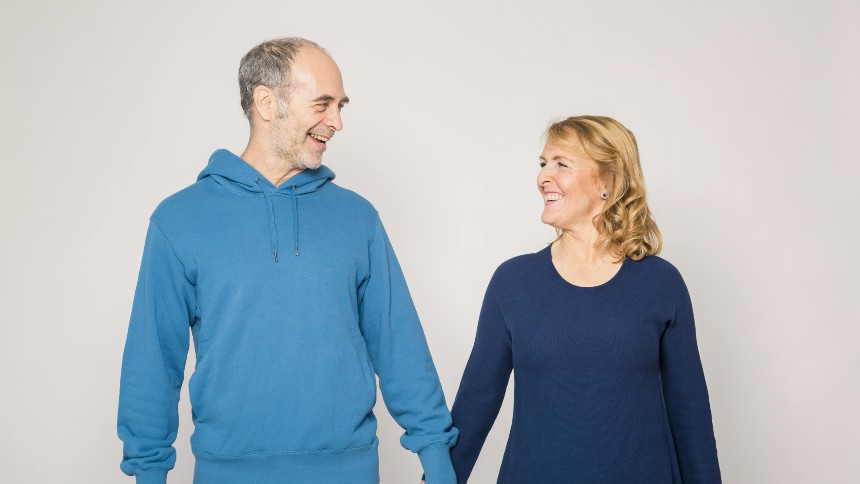 A Caucasian man and woman wearing blue-colored clothing hold hands while looking at one another. 