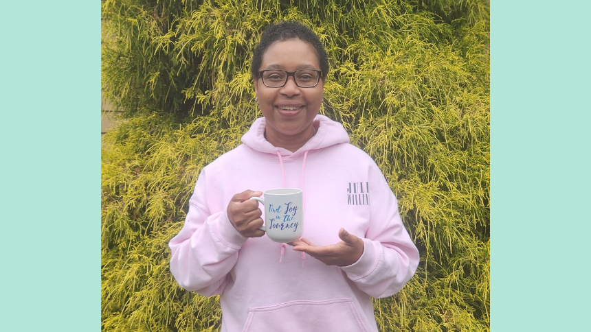 Leonie Roberts, a Norwalk Hospital breast cancer patient, standing outside, wearing a pink sweatshirt and holding a mug that says, “Find joy in the journey”.