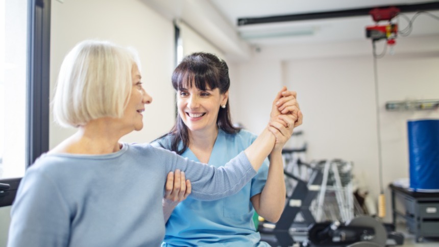 Young female occupational therapist is moving senior woman’s arm during therapy