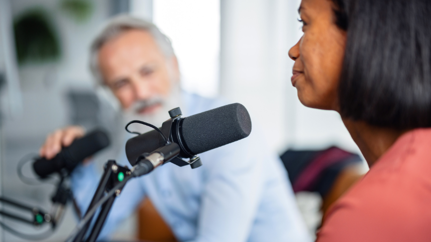 A mature Caucasian businessman and a mid-adult Black female colleague discussing topics on a podcast, equipped with high-quality microphones. 