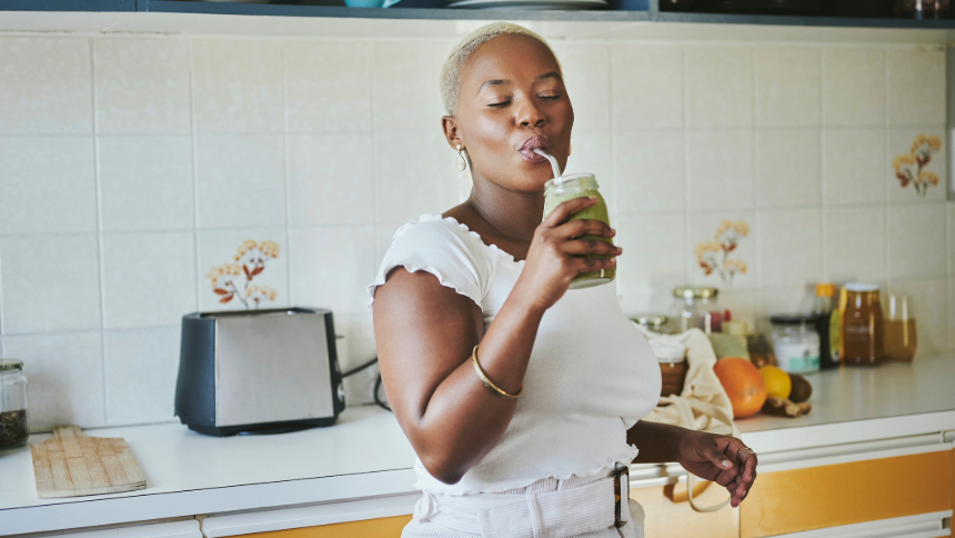 A young African woman standing with her eyes closed in her kitchen at home and drinking an organic smoothie with a reusable straw.