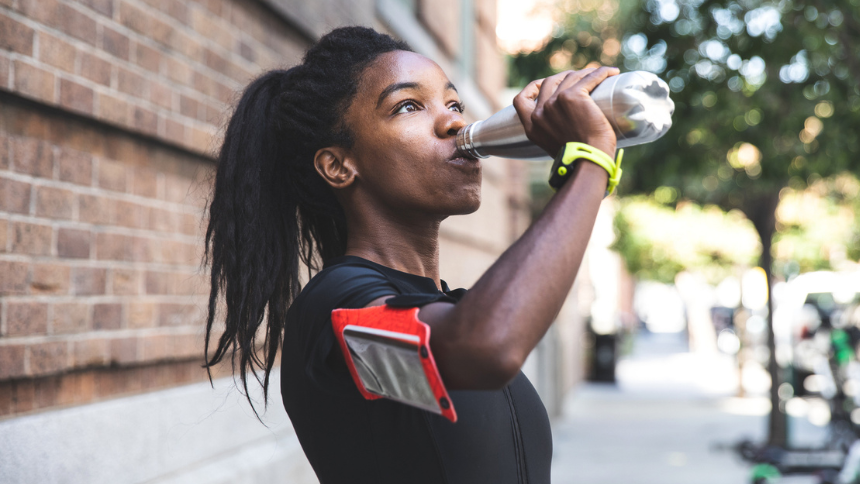 Woman exercising outdoors takes a break to drink from her water bottle 