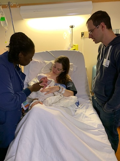 A mom holds her baby in a hospital bed surrounded by her husband and midwife.