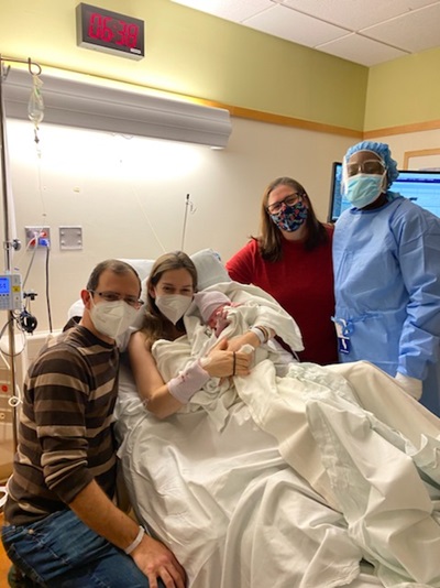 A mom holds her baby in a hospital bed surrounded by her husband, midwife and doula.