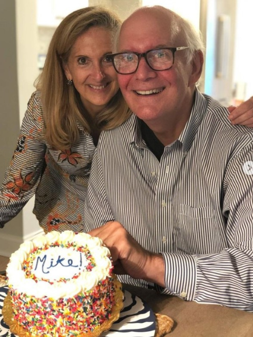 Lisa and Mike in front of a white frosted cake that says Mike on it to celebrate his birthday.