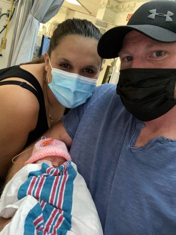 A mom and dad pose with a tiny newborn.