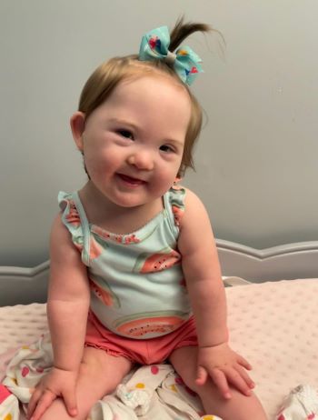 Chunky toddler sits up and smiles at camera.