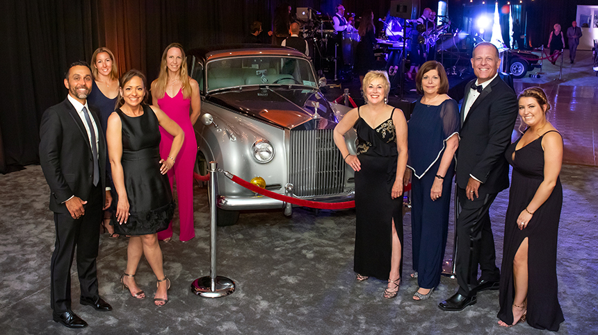 Doctors, nurses and caregivers pose for a portrait in front of a classic car.