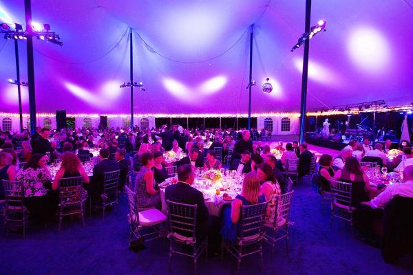 A grand ballroom tent and tables filled with people is lit up by purple lights