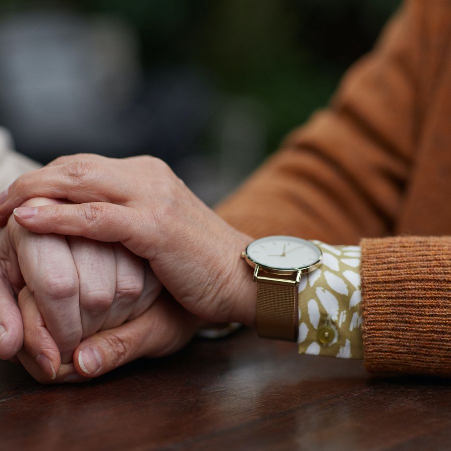 Man with orange sweater and watch holding woman's hand