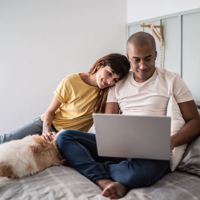 Young couple using a laptop while laying on a bed with a dog