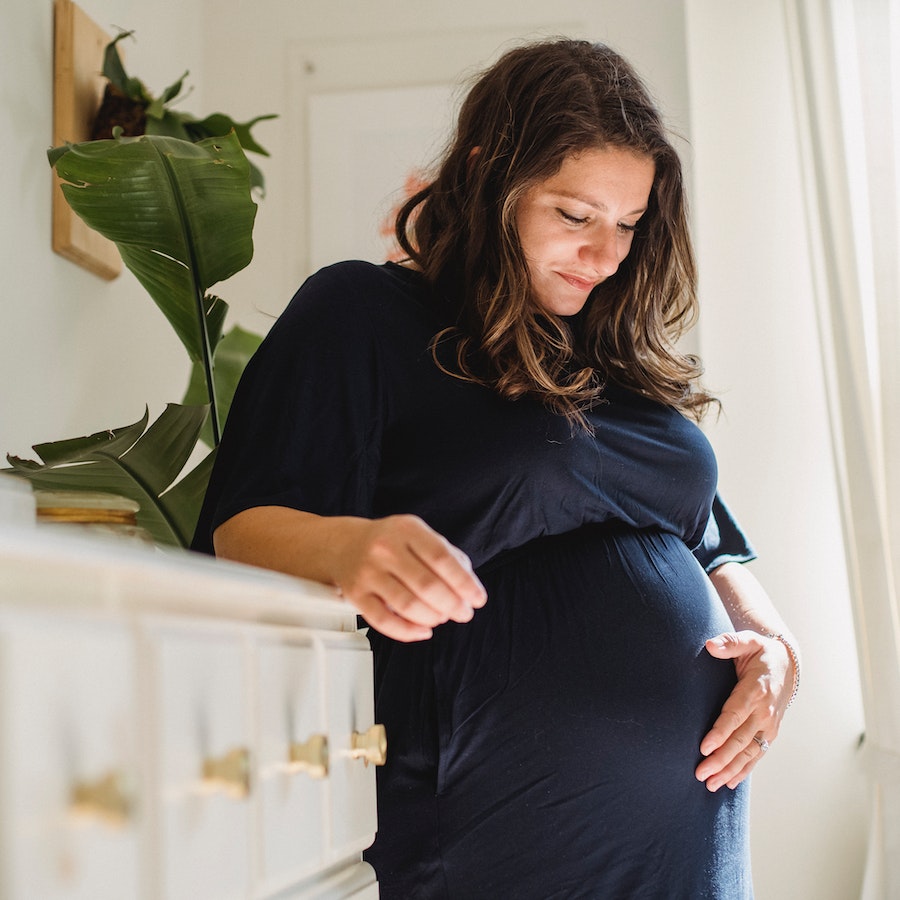 Smiling pregnant woman in blue dress holding her belly