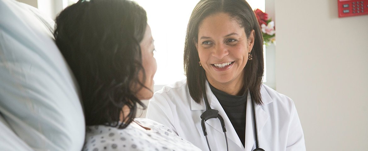 Woman doctor talks to female patient bedside