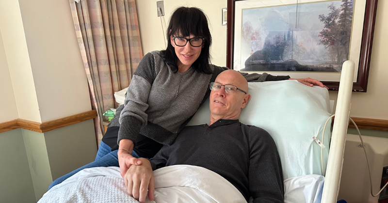 Michael relaxing in his hospital bed with Gloria beside him holding his hand.