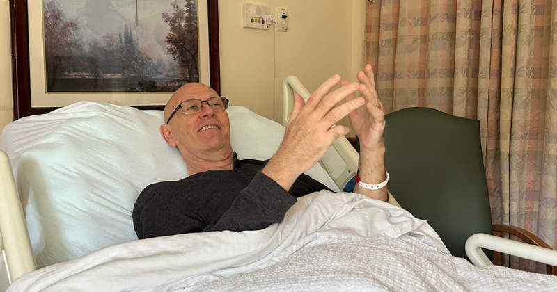 Michael relaxing in his hospital bed with his arms and hands raised, practicing tai chi.
