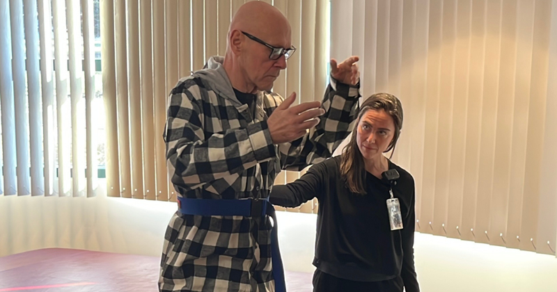 Michael standing, practicing tai chi with his occupational therapist beside him.