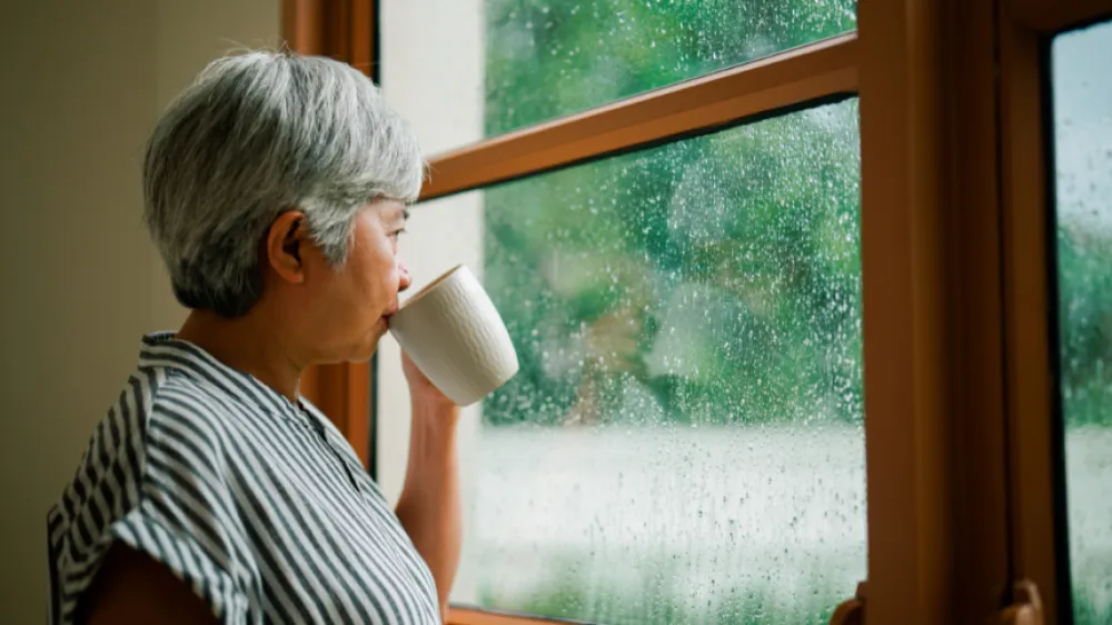 Woman standing by the window on a rainy day drinking coffee