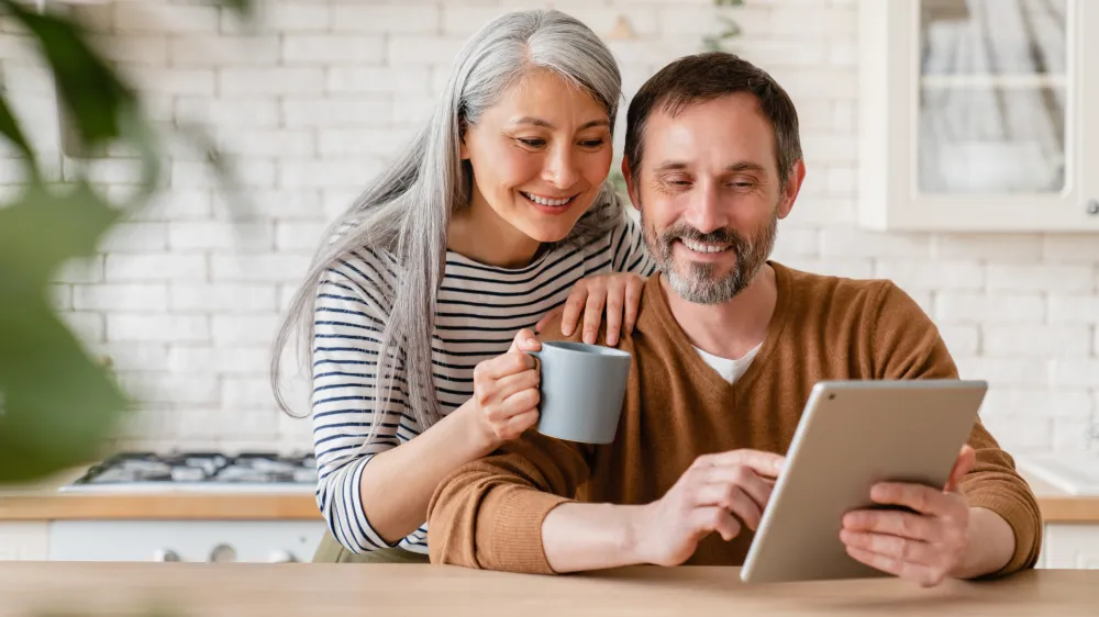 Happy mature middle-aged couple confirming that they booked their colonoscopy exam on a tablet during breakfast.