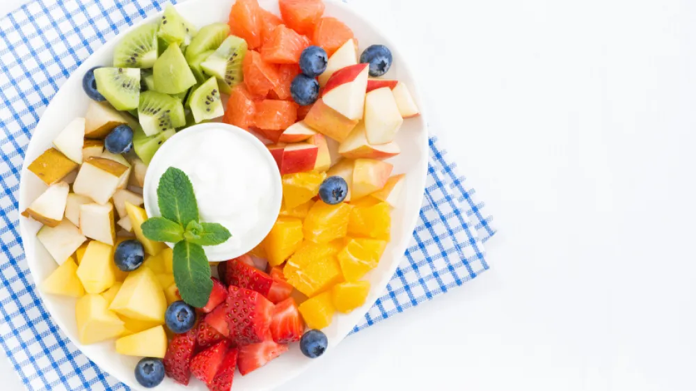 An overhead picture of a summer fruit salad on a blue and white checked napkin.