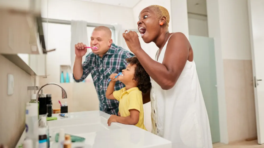 A happy mom, dad and their young son brushing their teeth in the bathroom and taking care of their oral health.