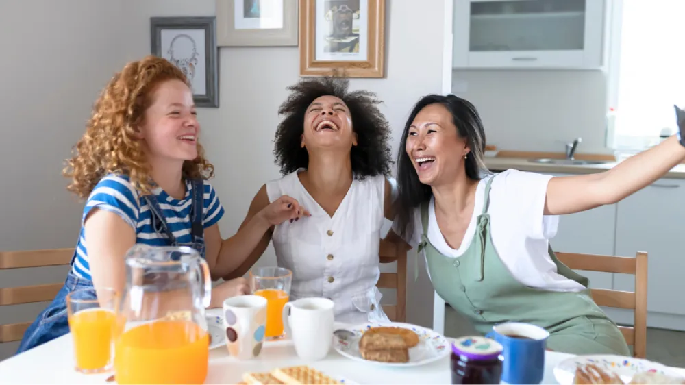 A group of friends laughing over brunch and taking a selfie.