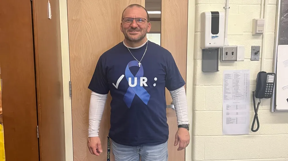 John Manganiello wearing a “check your colon” t-shirt in his high school classroom for Colorectal Cancer Awareness.
