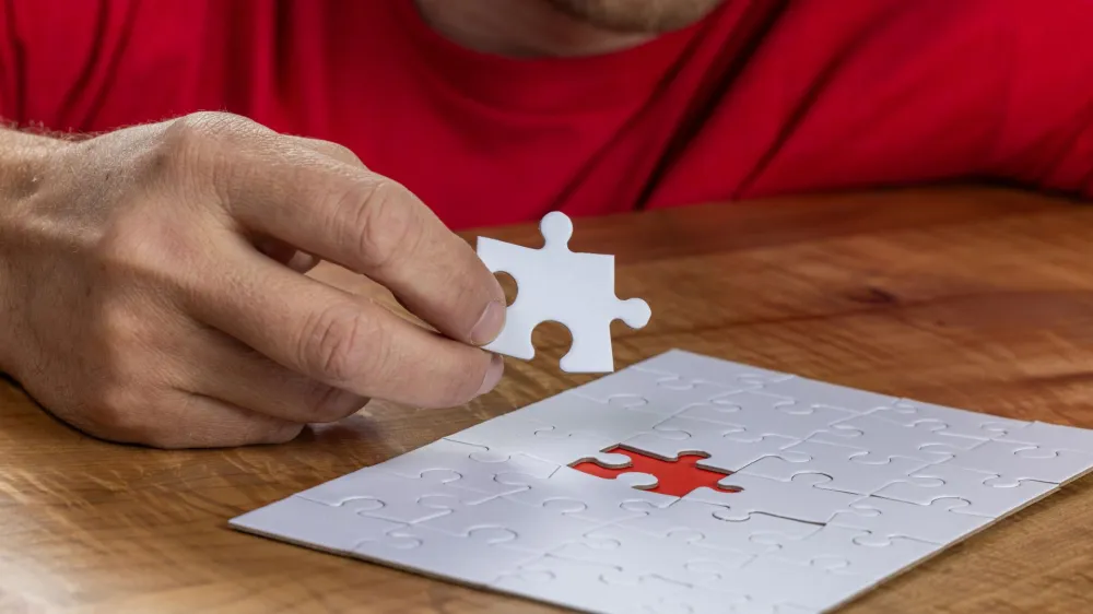 Blank puzzle with the missing piece being held next to the whole with a red placer where the last piece belongs. Concept for problem solving, like how the brain can rewire itself after a stroke.