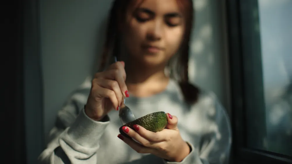 A young woman eating an avocado with a spoon. 