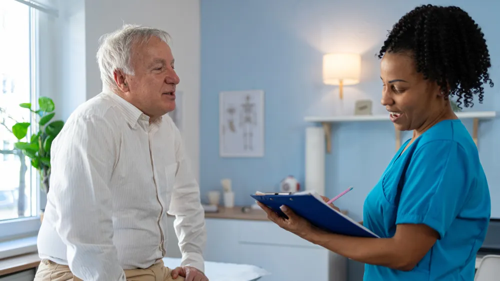 Man on an exam table talking about Parkinson’s disease with a nurse in a neurological office.
