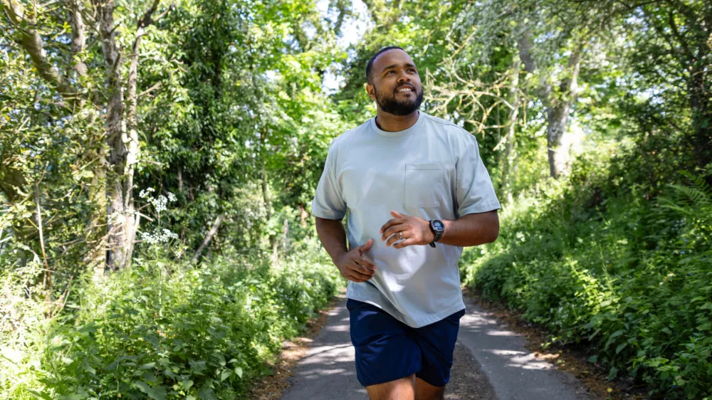 An adult man wearing sports clothing running outside on a footpath lined with lush foliage