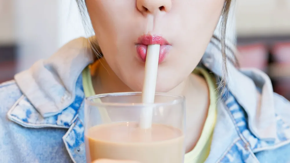 close up of a woman enjoying a glass of milk through a straw. 