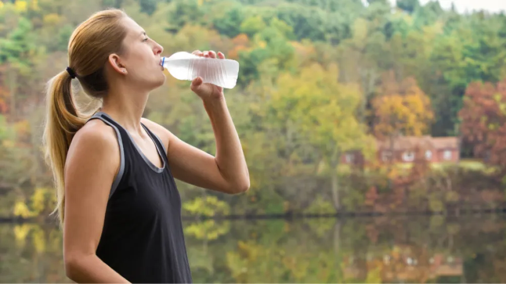 A woman stops for a drink of water on a beautiful fall day.