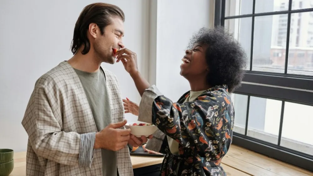 Hero - A Caucasian man and Black woman share a bowl of strawberries while smiling and eating